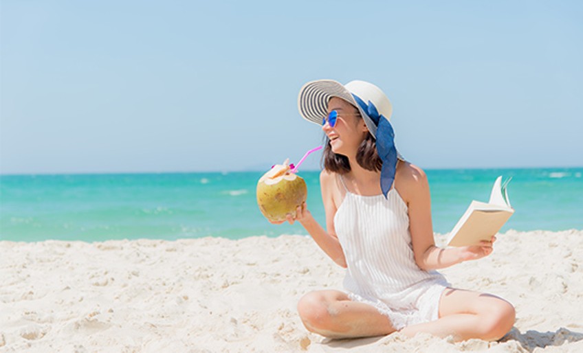 Resturlaub - Frau am Strand mit Buch und Kokosnuss 